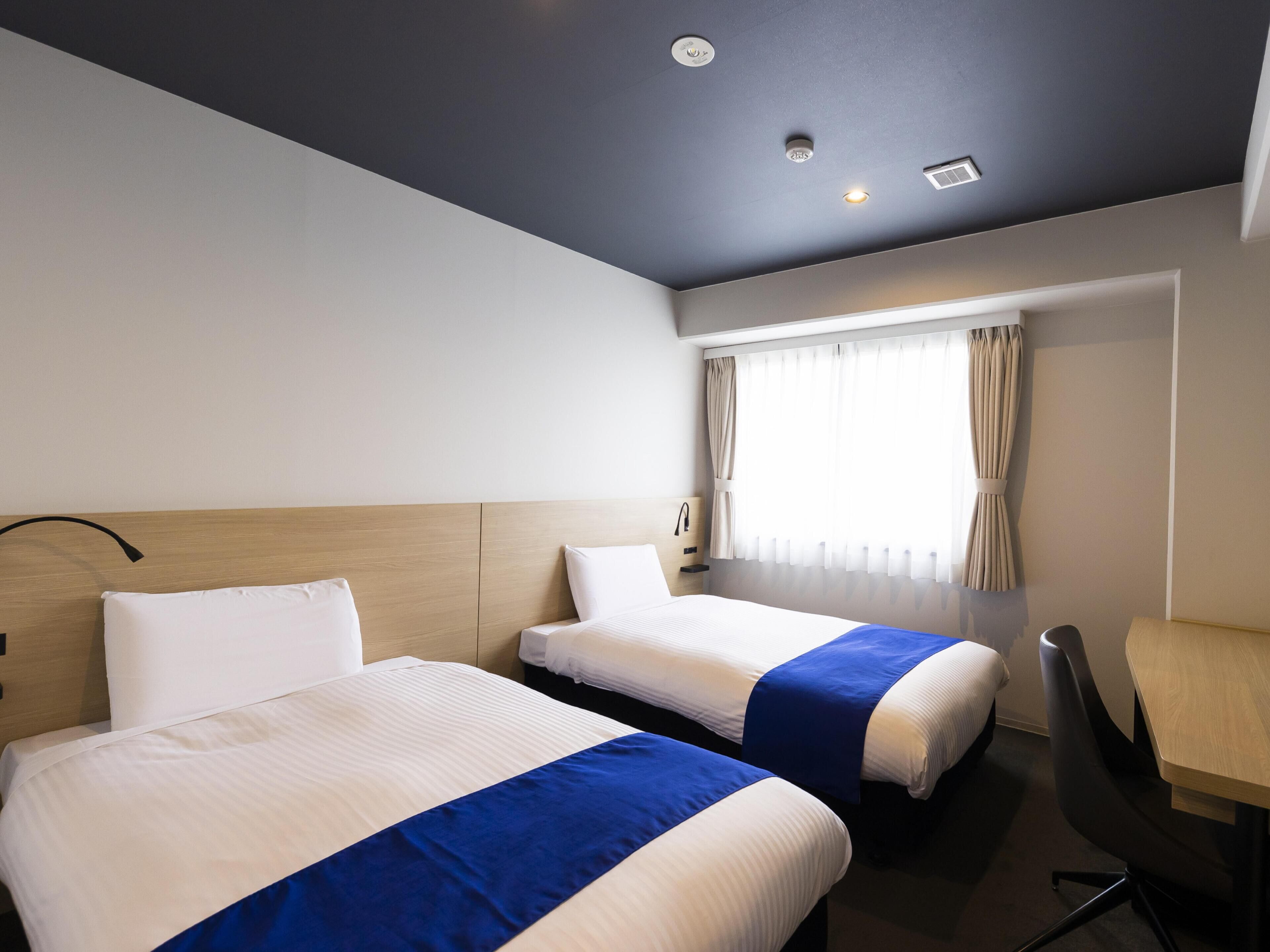 Hotellihuone, jossa on kaksi sänkyä, työpöytä ja ikkuna, jossa on verhot.
