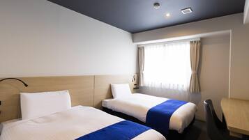 A hotel room with two beds, a desk, and a window with curtains.