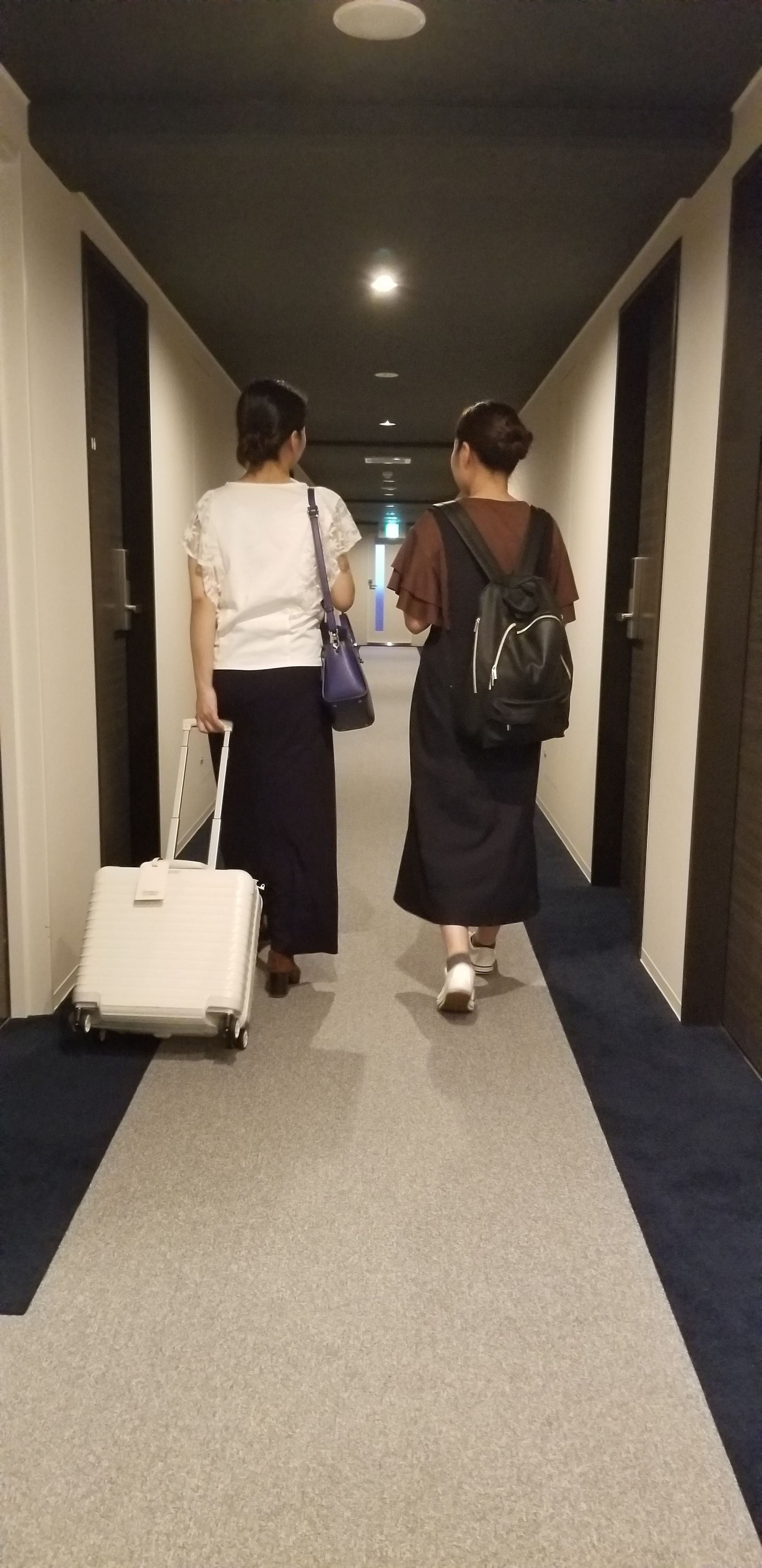 Un couloir d’hôtel avec un sol recouvert de moquette, des portes de chaque côté et un luminaire au plafond.