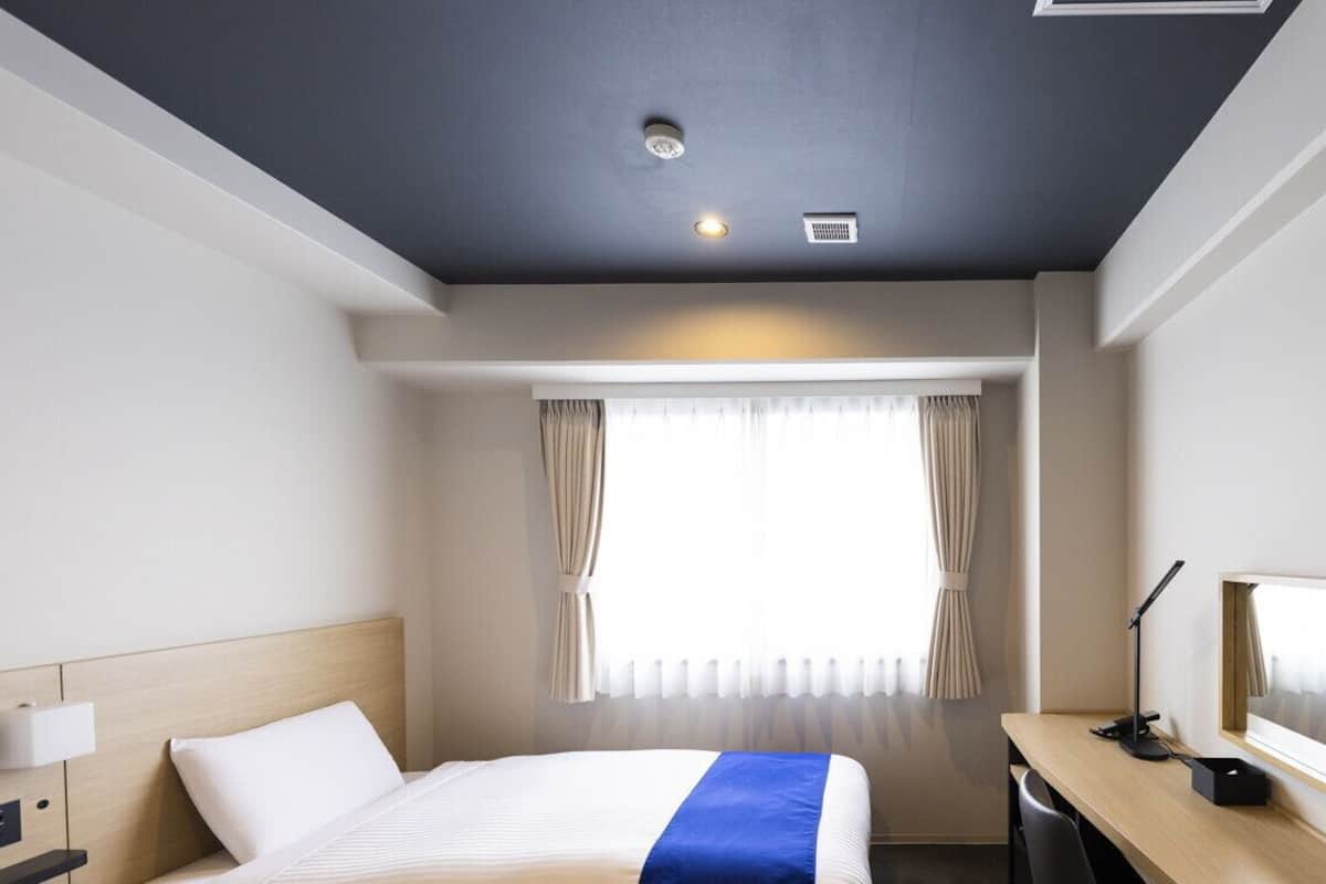 A hotel room with a bed, desk, lamp, and a window with curtains.