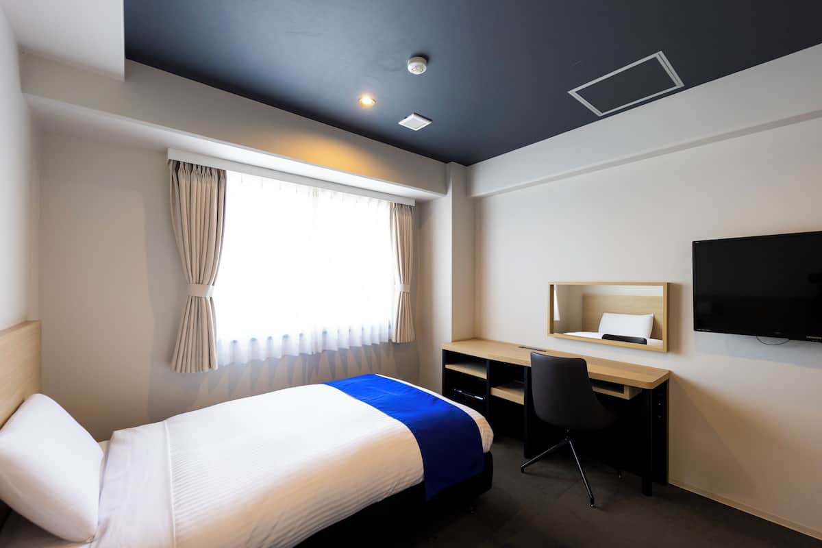 A hotel room with a bed, a desk, a chair, a TV, and a window with curtains.