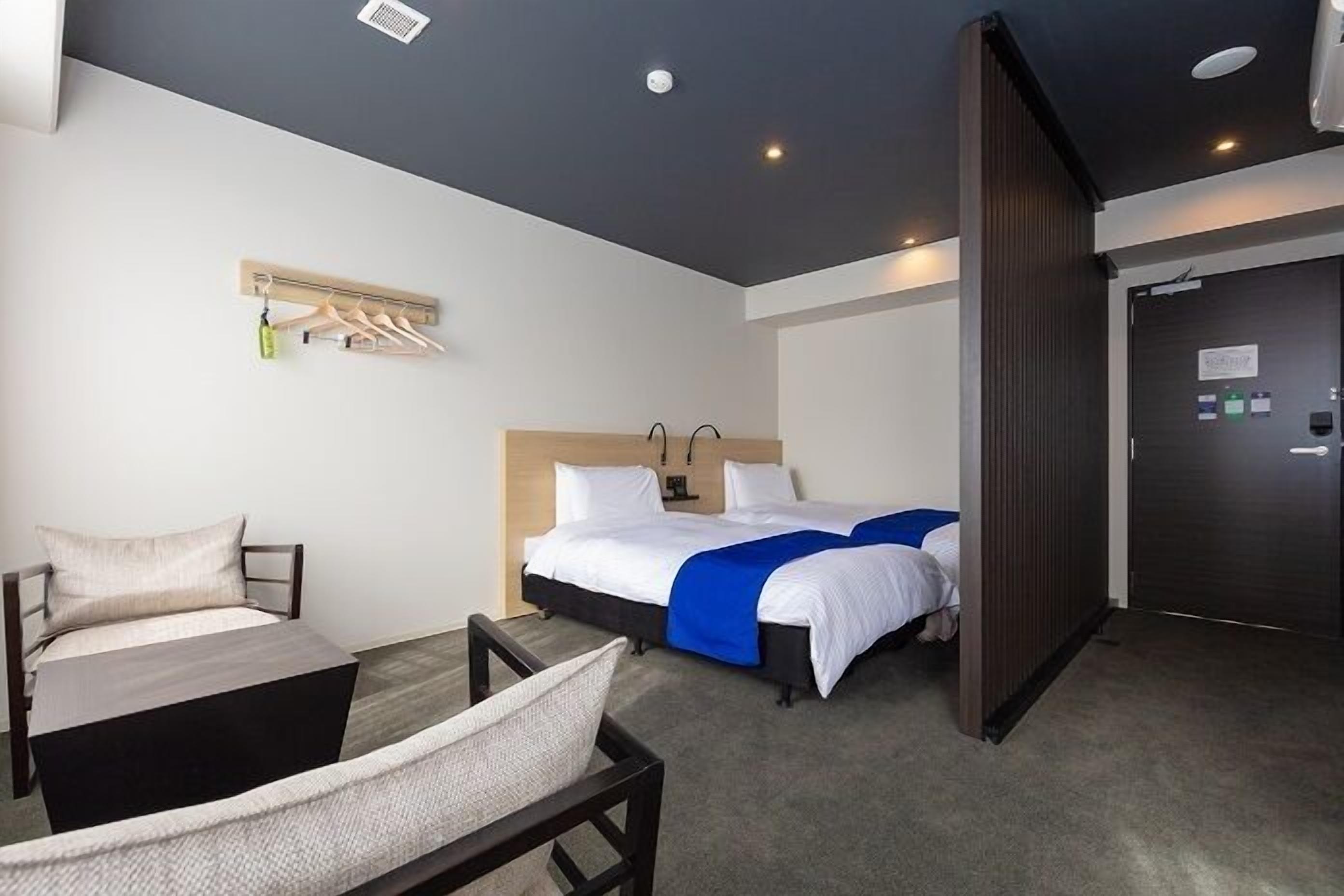 Quarto de hotel com cama, escrivaninha, cadeira, porta-roupas e porta.