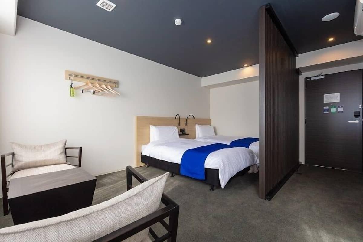 A hotel room with a bed, a desk, a chair, a coat rack, and a door.