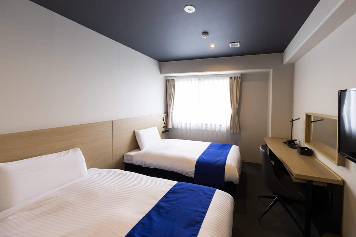A hotel room with two beds, a desk, a television, and a window with curtains.