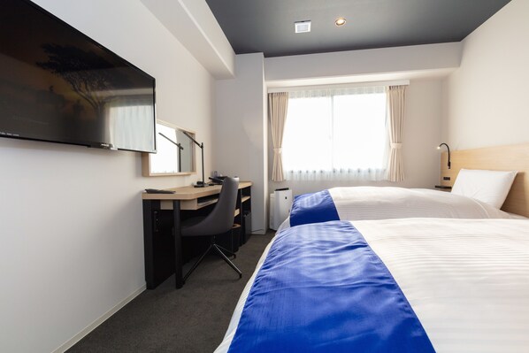 A hotel room with two beds, a desk, a chair, a flat-screen TV, and a window with curtains.