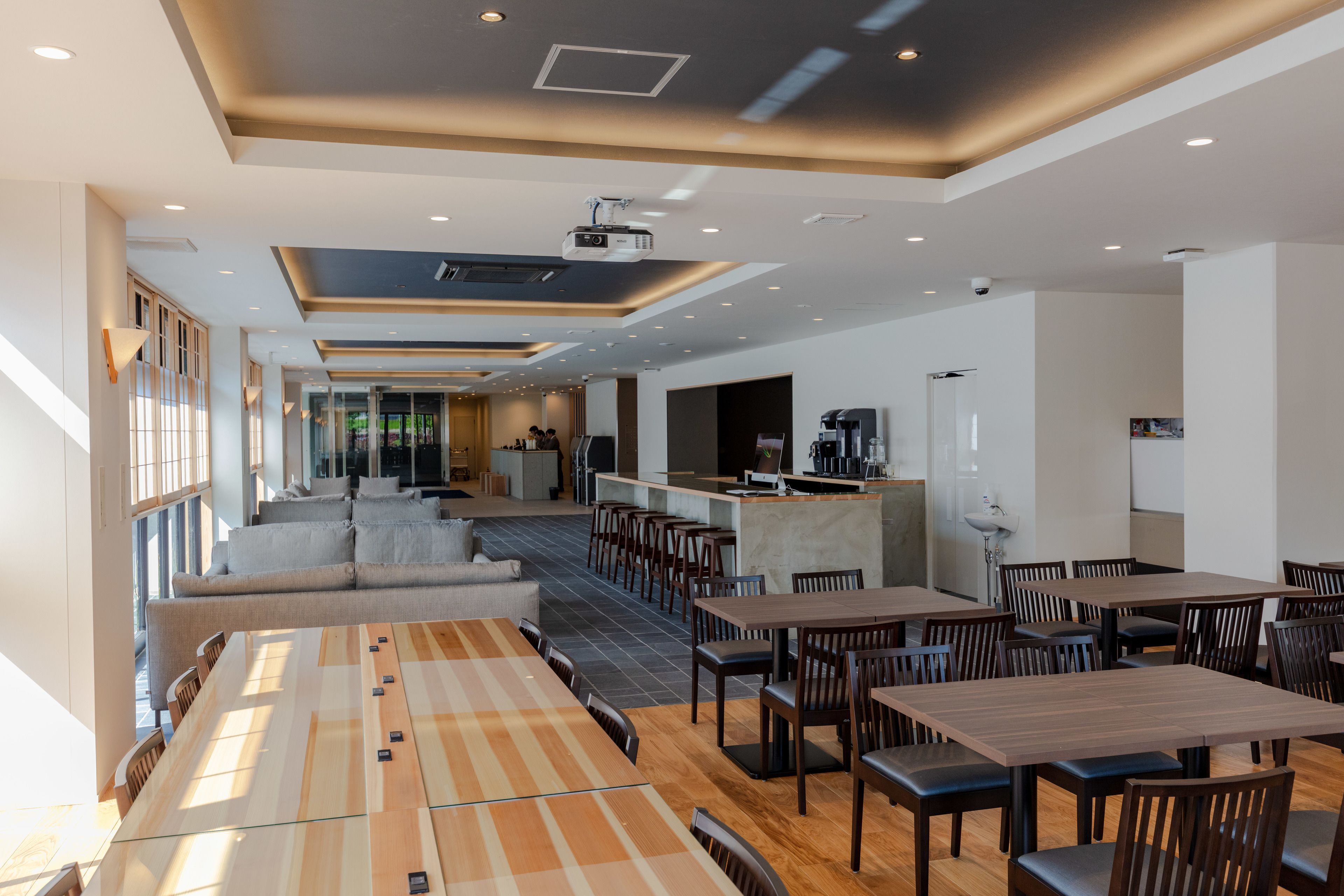A modern dining area with long tables and chairs, a bar area, and a seating area with sofas.