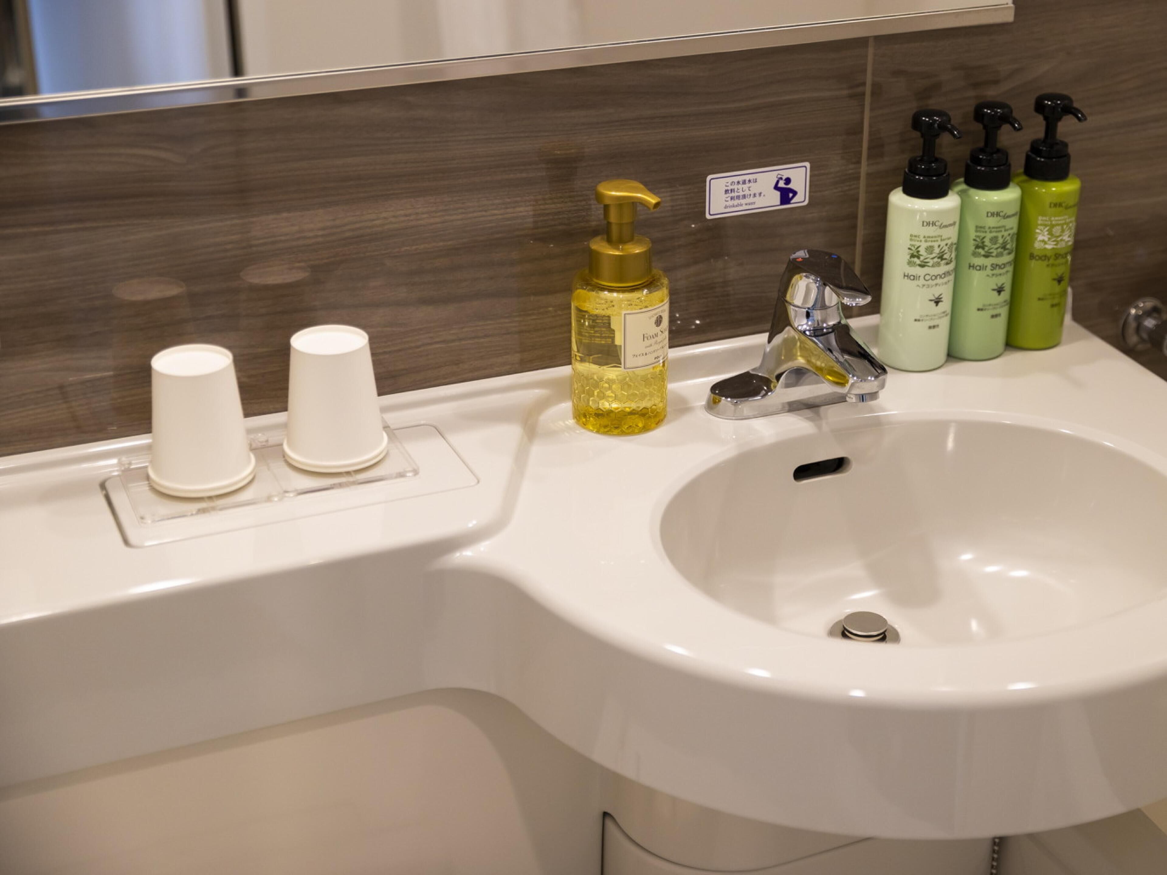 Un lavabo de baño con espejo, un dispensador de jabón dorado y tres botellas de productos para el cuidado corporal.