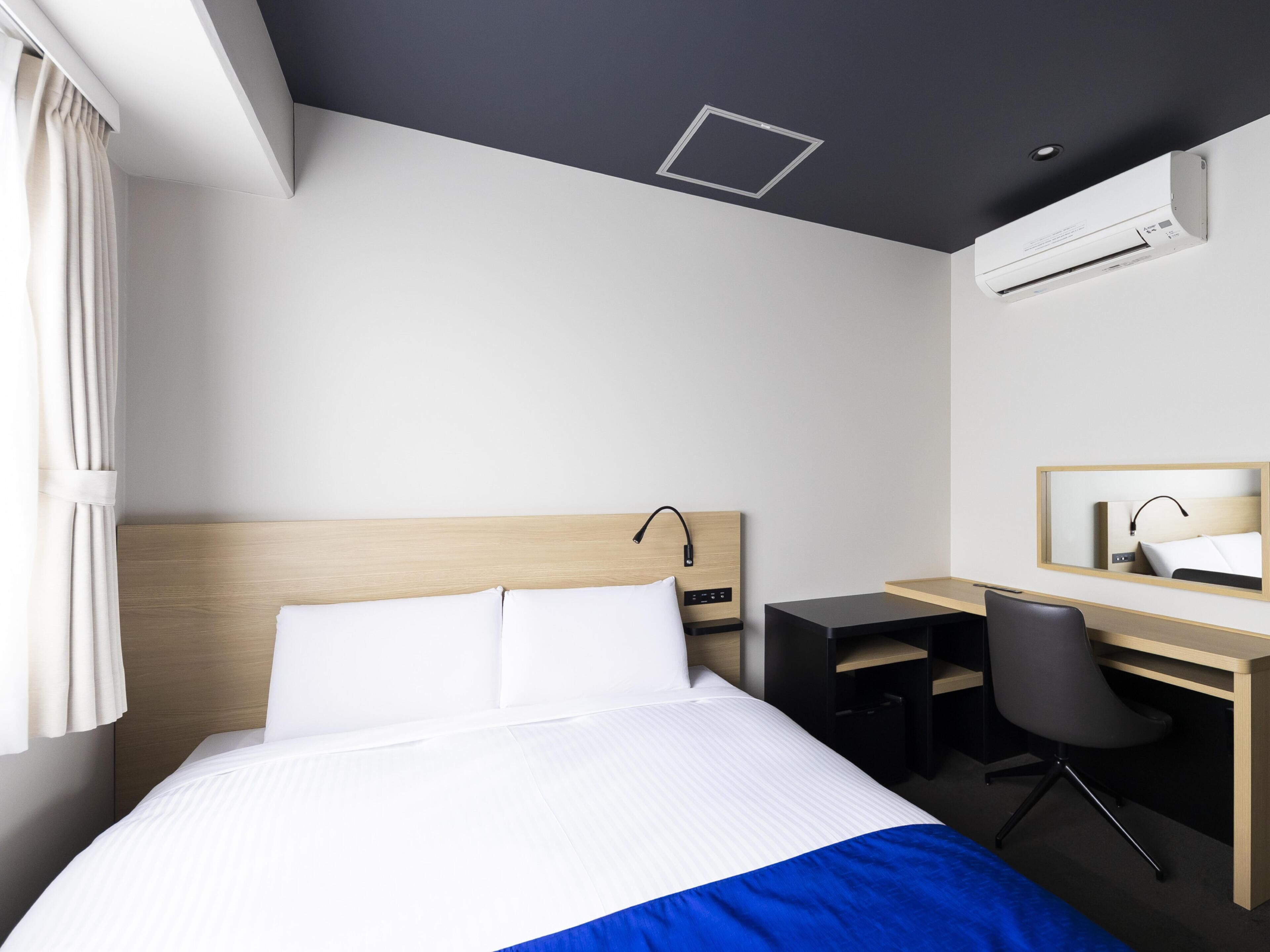 Ein modernes Hotelzimmer mit Bett, Schreibtisch, Stuhl und Klimaanlage.