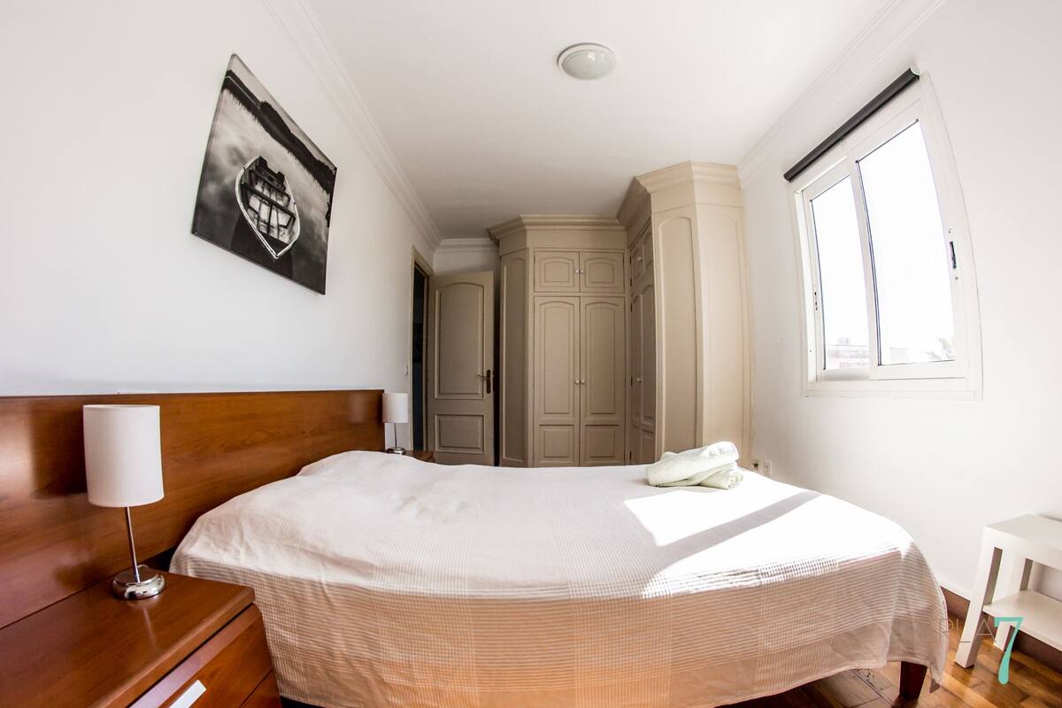 Een hotelkamer met een bed, nachtkastje, lamp, kledingkast en raam.