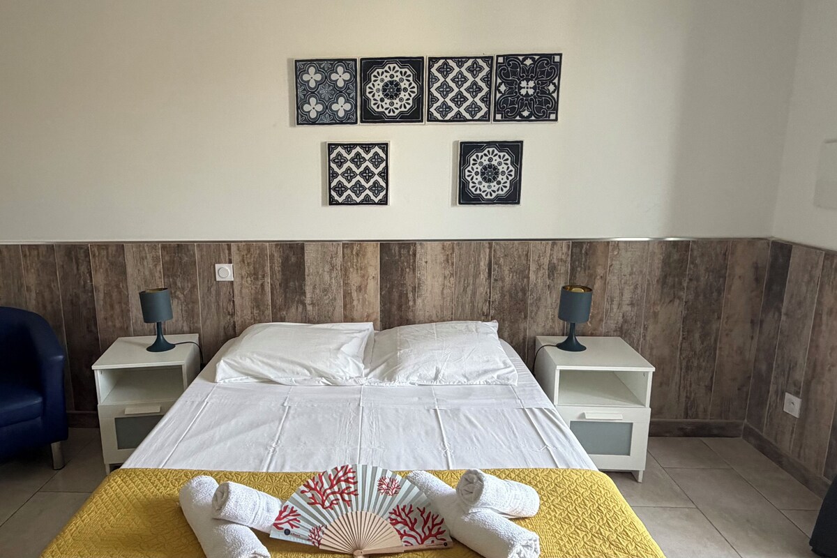 Una habitación de hotel con cama, dos mesitas de noche, una silla azul y decoración en la pared.