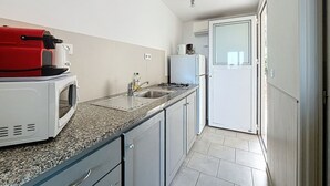 A narrow kitchen with a microwave, a red appliance, and a refrigerator. - Les Pavillons du Belvédère (Porto-Vecchio)