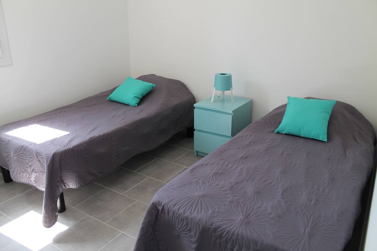 Two single beds with matching headboards and footboards, a small bedside table with a lamp, and a wall-mounted light fixture.