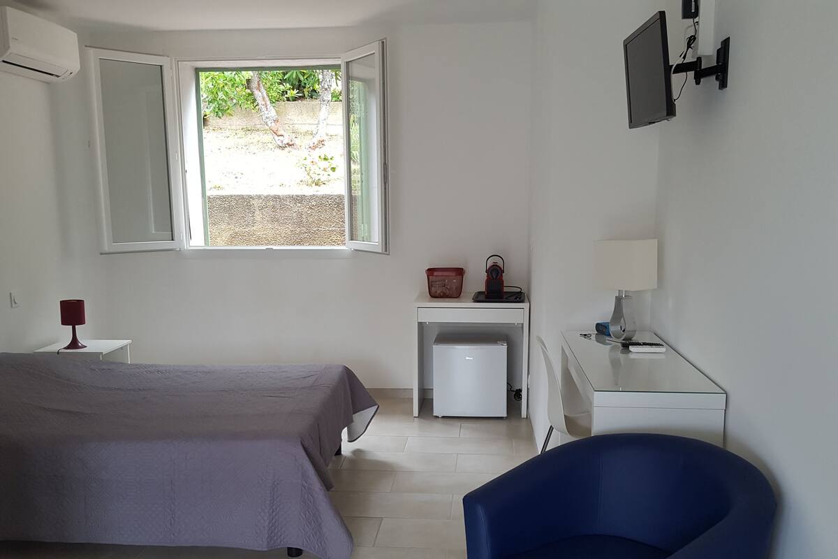 A bedroom with a bed, a desk, a chair, a window, and a small refrigerator.
