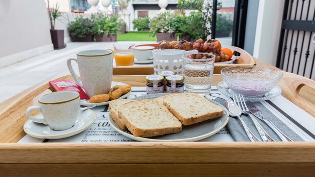 Bandeja de desayuno con pan, mantequilla, mermelada y un bol de fruta en un balcón con vistas a un jardín y edificios.