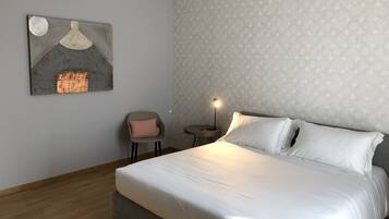 Ein ordentlich eingerichtetes Schlafzimmer mit einem großen Bett, einem kleinen Nachttisch, einem Sessel und einem Wandbild.