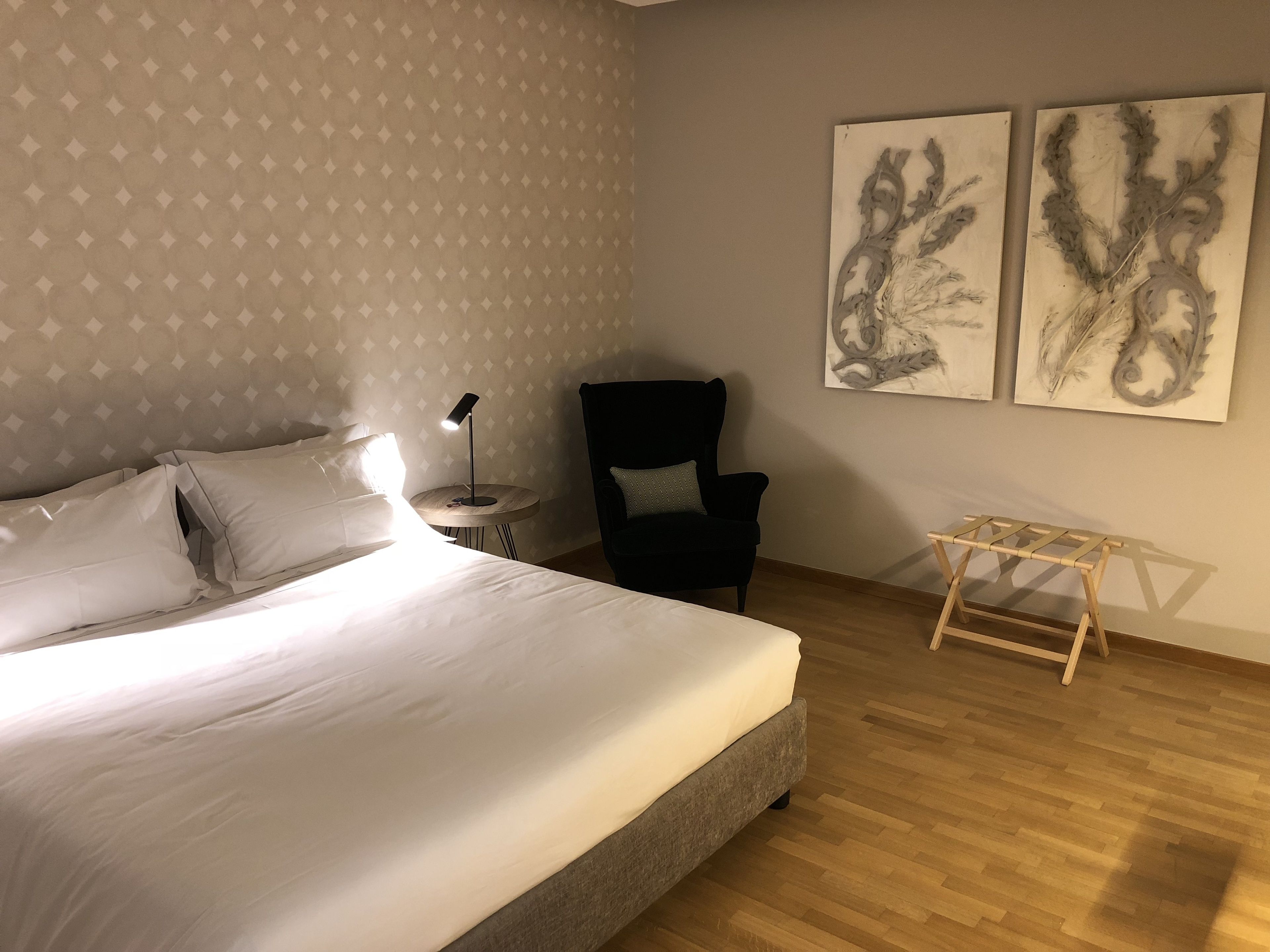 A hotel room with a bed, a chair, a small table, and two wall-mounted artworks.