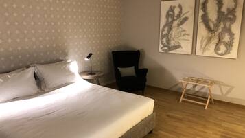 A hotel room with a bed, a chair, a small table, and two wall-mounted artworks.