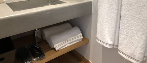 A bathroom with a large sink, two faucets, a mirror, and a towel rack with two towels.