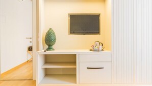 Una habitación moderna y minimalista con un escritorio blanco, un televisor de pantalla plana montado en la pared y un jarrón verde decorativo sobre el escritorio.