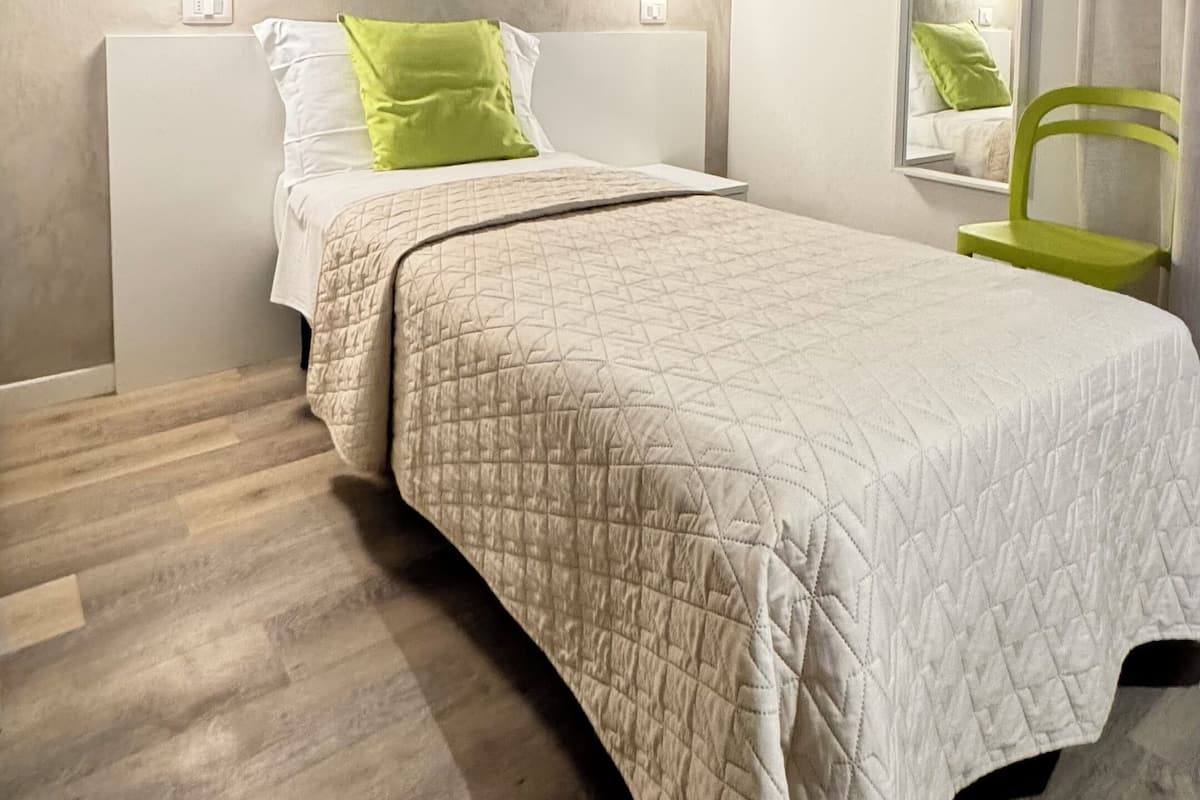 A modern bedroom with a bed, bedside lamps, a round mirror, and a chair.