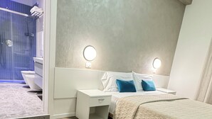 A modern bedroom with a large bed, a nightstand, a bedside table, and a bathroom visible through an open door. - Hotel Cristina (Jesolo)