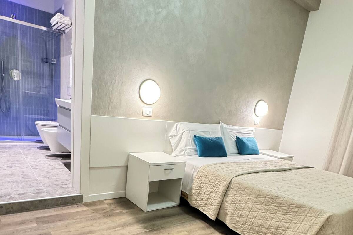 A modern bedroom with a large bed, a nightstand, a bedside table, and a bathroom visible through an open door.
