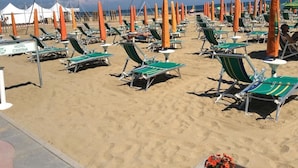A beach with rows of green and white sun loungers, orange beach umbrellas, and a sign for Hotel Cristina. - Hotel Cristina (Jesolo)