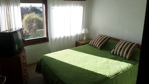 Ein Schlafzimmer mit Bett, Nachttisch, Lampe, Kommode und Fernseher.