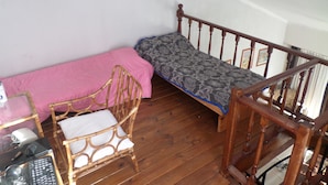 Ein kleines Zimmer mit einem Einzelbett, einem Holzstuhl und einem Schreibtisch mit einem Computer.