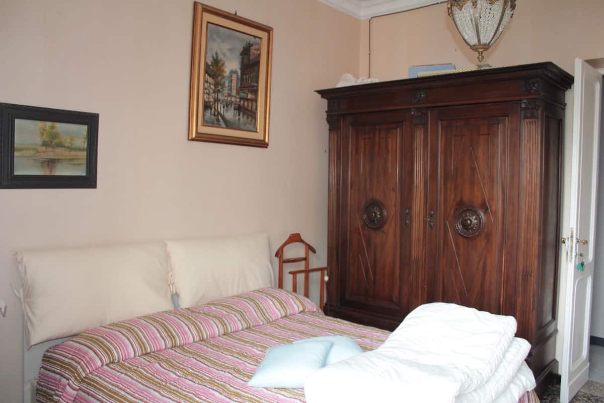 A bedroom with a bed, a wooden wardrobe, and two framed pictures on the wall.