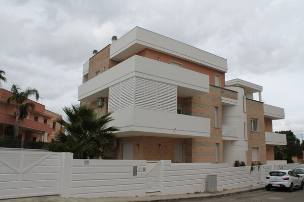 A modern two-story residential building with a white exterior, a balcony on the upper floor, and a gated entrance. - Aries B&B (Casarano)