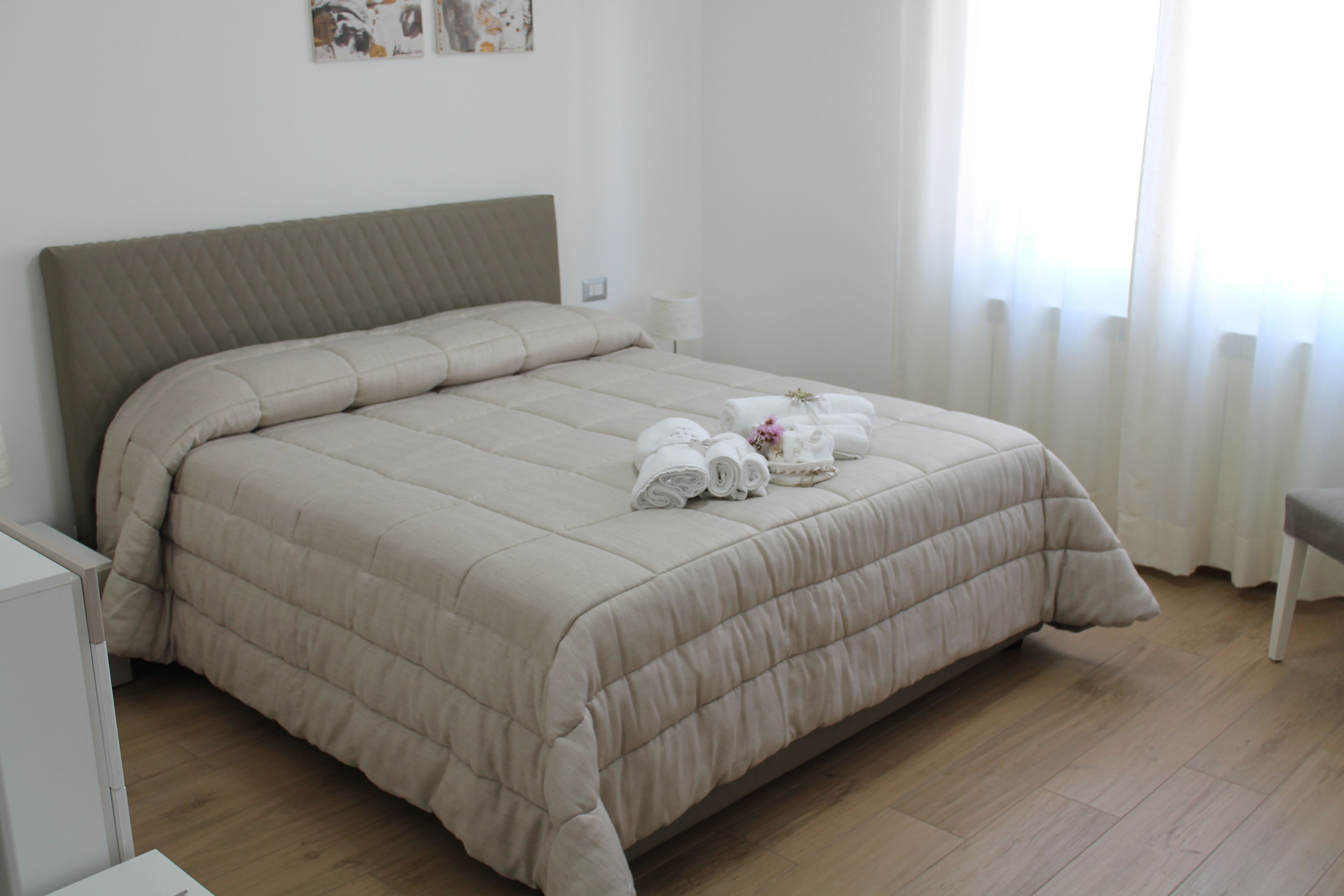 Un lit bien fait, recouvert d’une courtepointe beige, une table de chevet avec une lampe et une chaise.