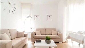 A modern living room with a beige sofa, a white coffee table, and a dining area with a white tablecloth. - Aries B&B (Casarano)
