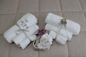 Two neatly folded white towels with "R&B ARIES" embroidered on them, tied with a ribbon, and placed on a beige sofa. - Aries B&B (Casarano)