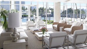 A spacious living area with a view of a waterfront, featuring a sofa, chairs, a coffee table, and a lamp. - Grand Beach Hotel Bay Harbor (Bay Harbor Islands)