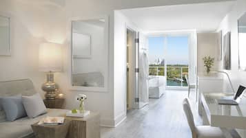 A modern hotel room with a balcony, a sofa, a desk, and a mirror.