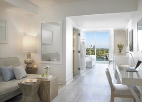 Una habitación de hotel moderna con balcón, un sofá, un escritorio y un espejo.