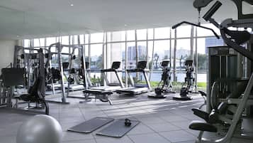 A gym with various exercise equipment, large windows, and a view of a body of water and buildings.