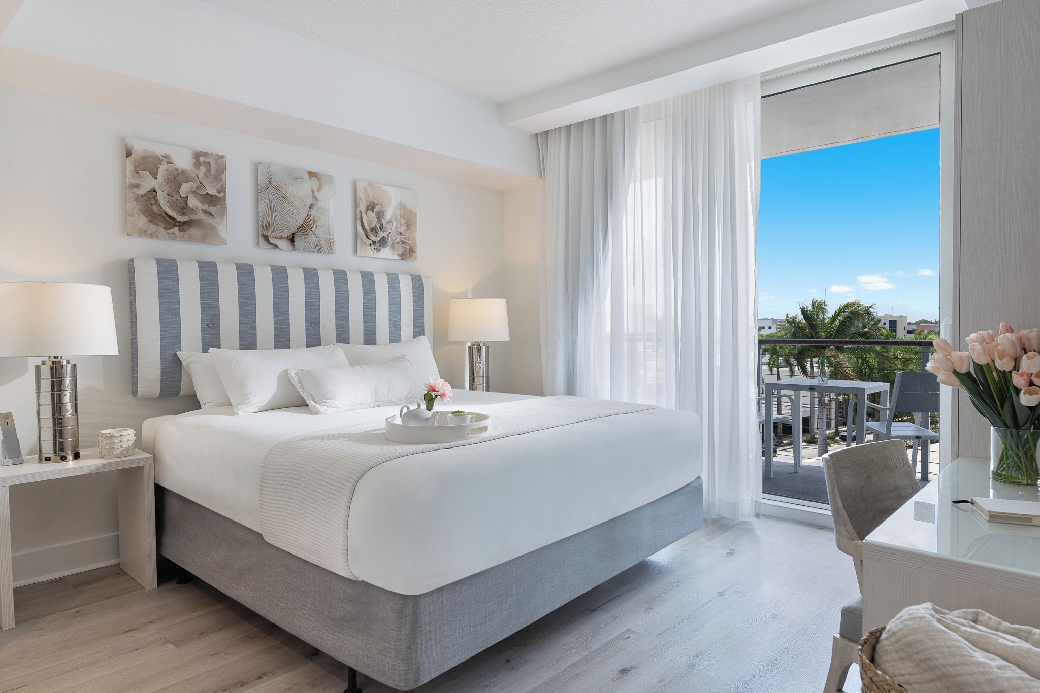 A hotel room with a large bed, two bedside tables, a nightstand, a window with curtains, and a view of the outdoors.