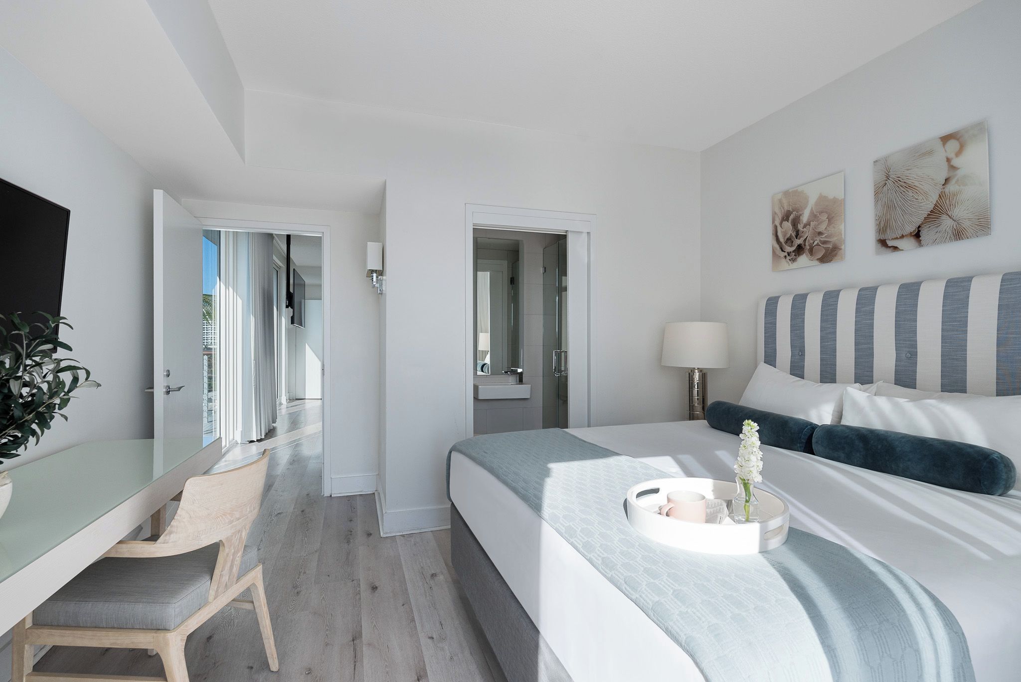 Ett modernt hotellrum med en säng, ett sängbord, en stol och utsikt över korridoren.