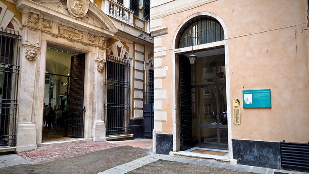 L’entrée d’un bâtiment historique, ornée de sculptures complexes, avec une porte en verre et une plaque commémorative.
