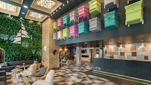 A modern lobby with a geometric patterned floor, a green wall with a tree decoration, and colorful storage units. - Arte Spa & Park Hotel (Velingrad)