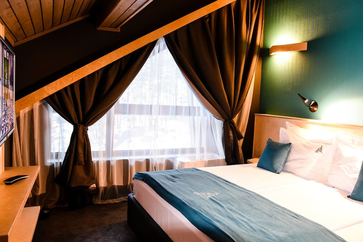 A bedroom with a bed, a desk, a chair, and a window with curtains.