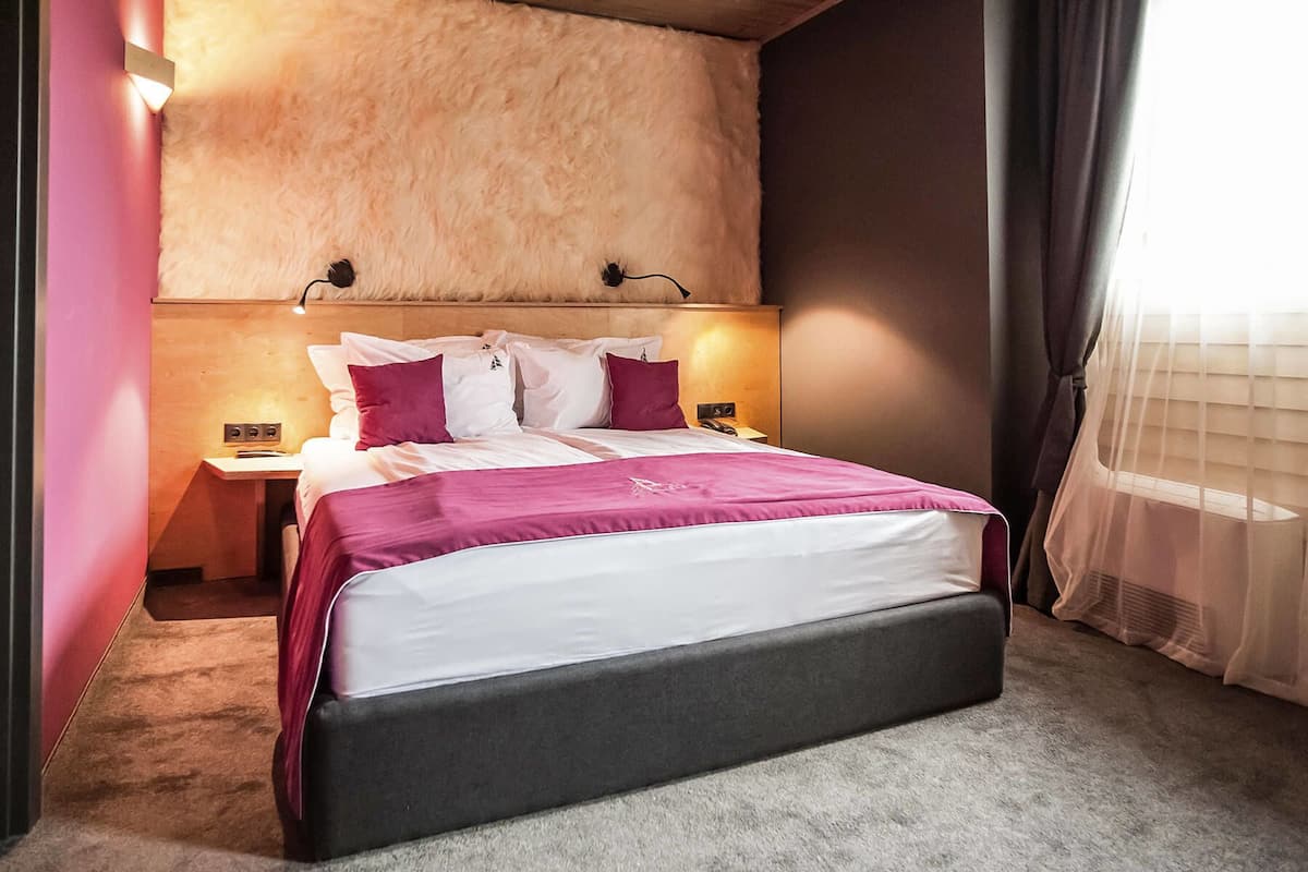 A neatly made bed with a white and pink bedspread, two nightstands with lamps, and a headboard with a fur-like texture.