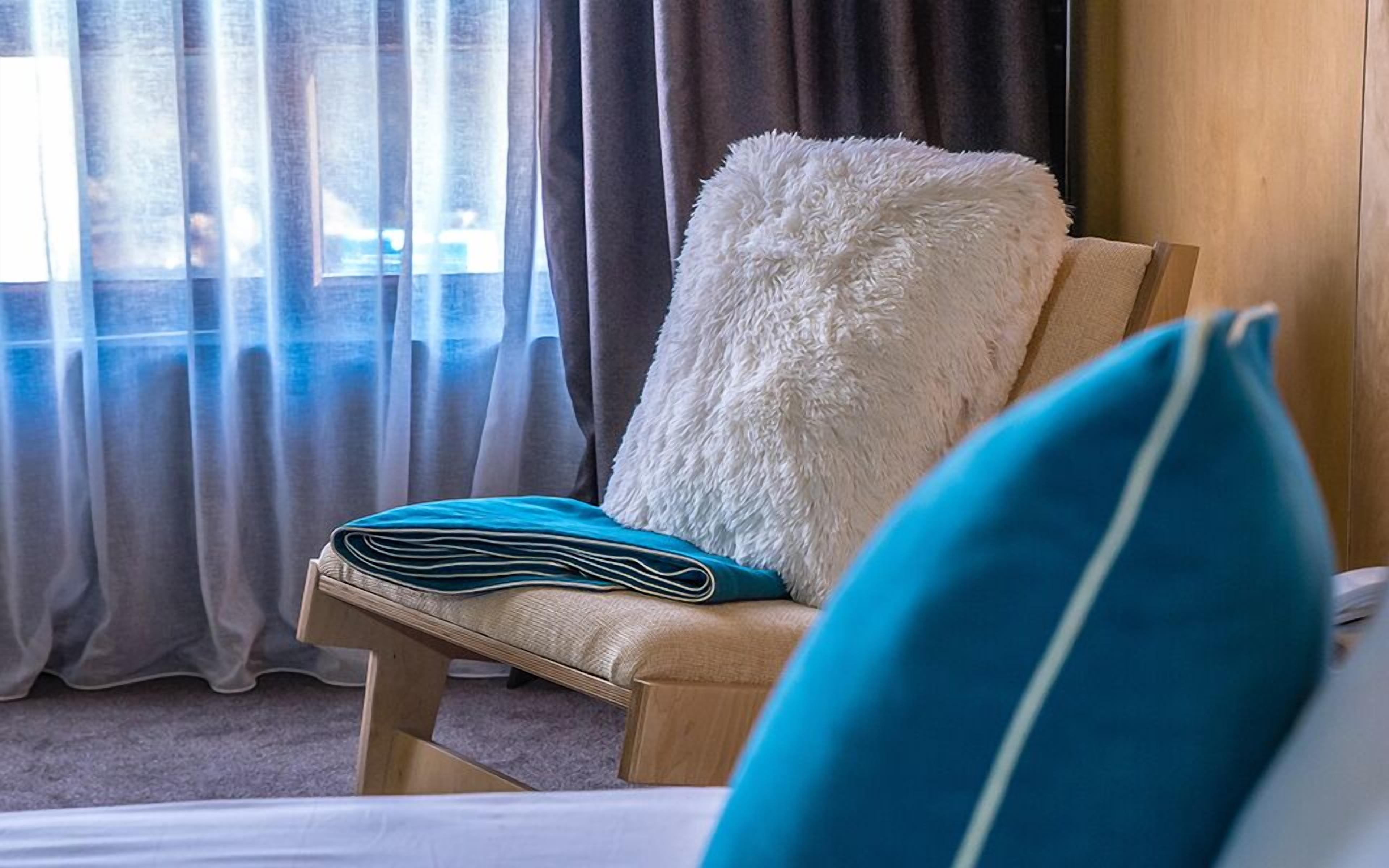 A hotel room with a wooden chair, a white fluffy pillow, and a blue pillow.