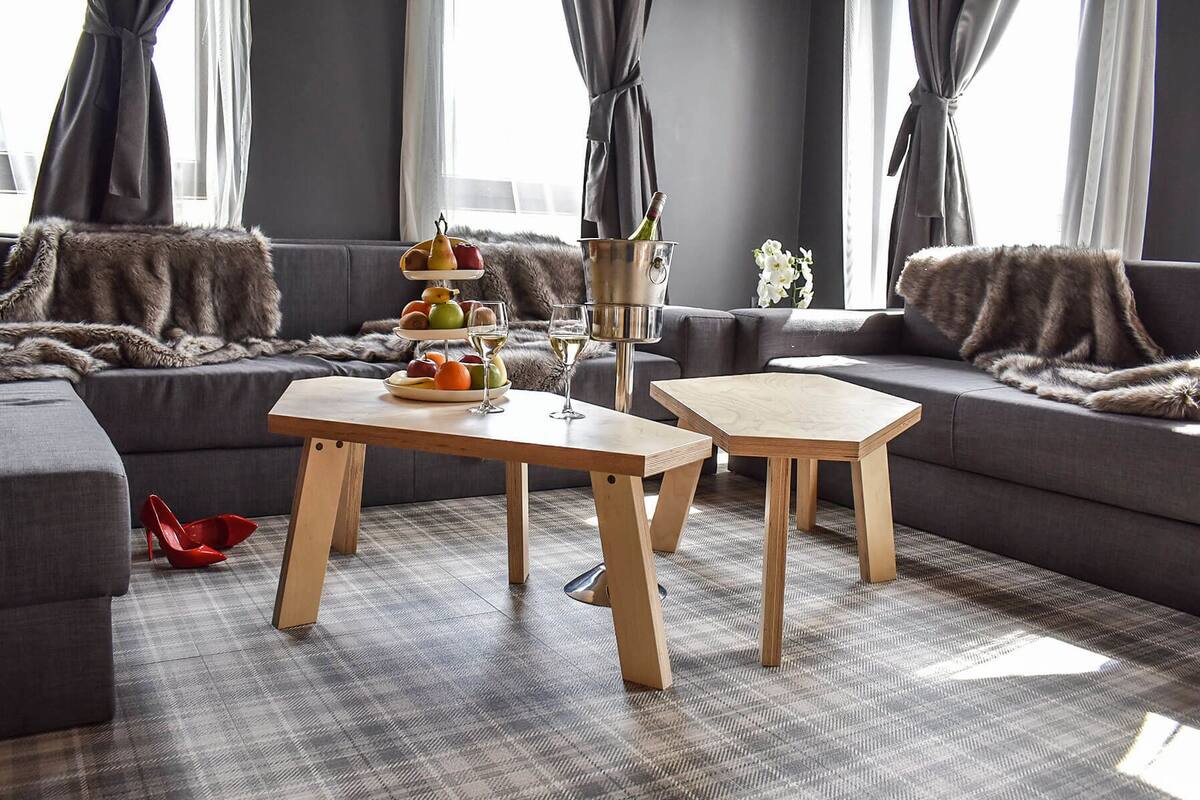 A modern living room with a grey sofa, a wooden coffee table, and a small side table. There is a fruit platter and wine glasses on the coffee table.