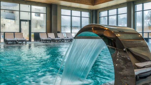 An indoor swimming pool with a waterfall feature, lounge chairs, and large windows. - Arte Spa & Park Hotel (Velingrad)
