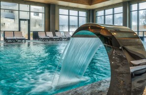 An indoor swimming pool with a waterfall feature, lounge chairs, and large windows. - Arte Spa & Park Hotel (Velingrad)