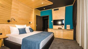 Habitació d'hotel moderna amb un capçal de llit de fusta, un llit amb roba de llit blanca i blava, una taula de treball amb televisió de pantalla plana i una paret d'accent color aquamarina.