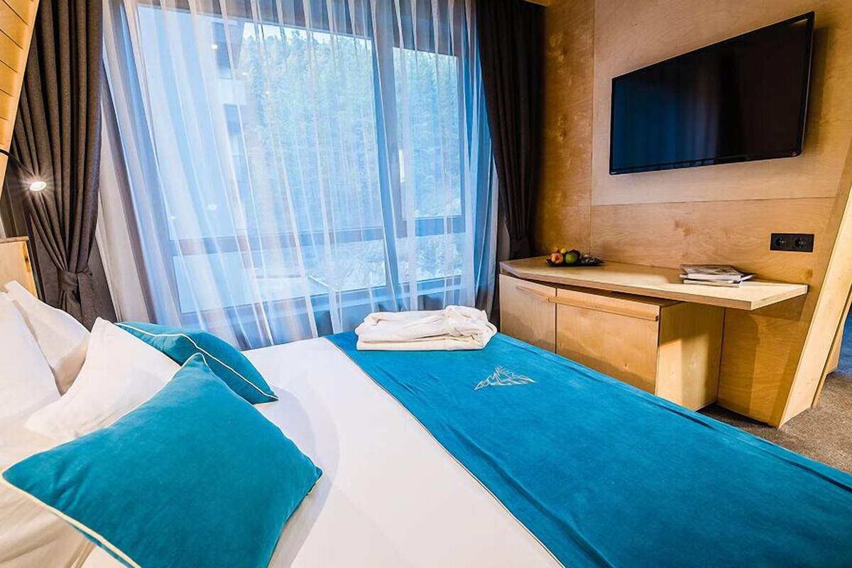A hotel room with a bed, a desk, a TV, and a window with curtains.